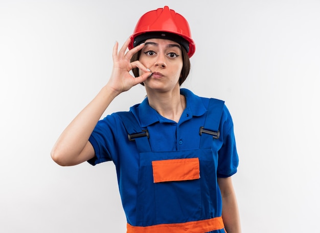 Looking at camera young builder woman in uniform showing delicious gesture 