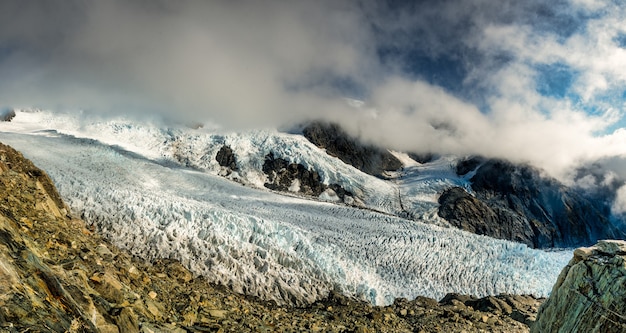 Looking over the edge down into to Franz Josef Glacier below and the mountains with cloudy sky