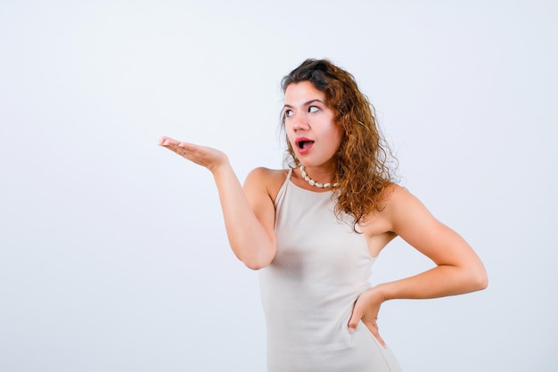 Looking left girl is pointing left with hand and putting other hand on waist on white background