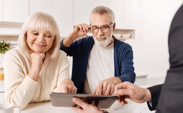 Looking at our future house project. Smart capable educated real estate agent working with retired couple of clients while demonstrating project of the house and using device