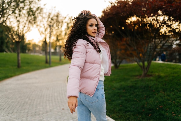 Looking over the shoulder of someone looking in the park is a beautiful girl in a warm jacket and jeans