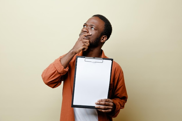 Looking at side grabbed chin young african american male holding clipboard isolated on white background