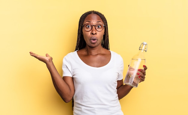 Looking surprised and shocked, with jaw dropped holding an object with an open hand on the side. water bottle concept