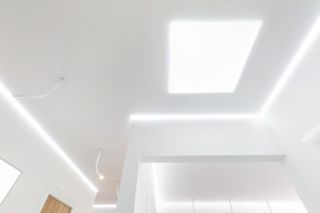 Looking up on suspended ceiling with halogen spots lamps and drywall construction in empty room in apartment or house Stretch ceiling white and complex shape