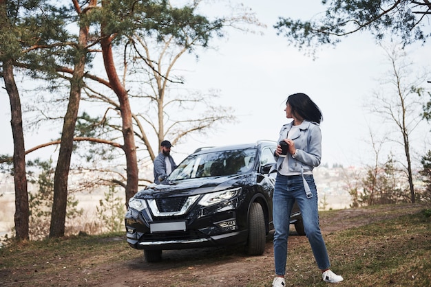 Looks behind at boyfriend. Couple have arrived to the forest on their brand new black car