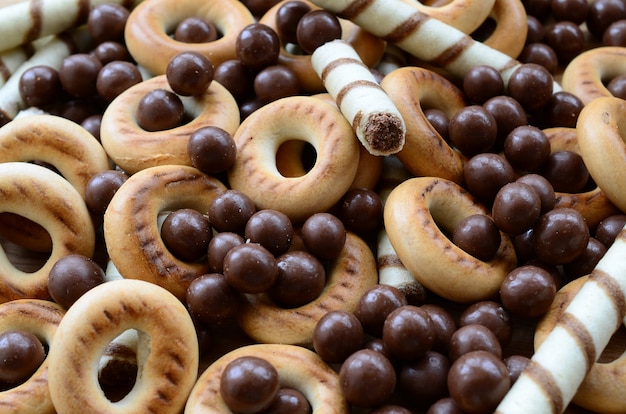 A lot of crispy sweet tubules, chocolate melting balls and yellow bagels lie on a wooden surface