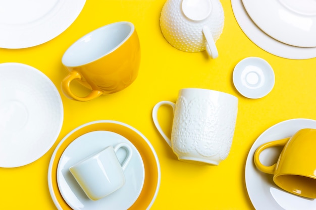 A lot of different ceramic dishes, empty coffee pairs, plates, cups on a bright yellow background