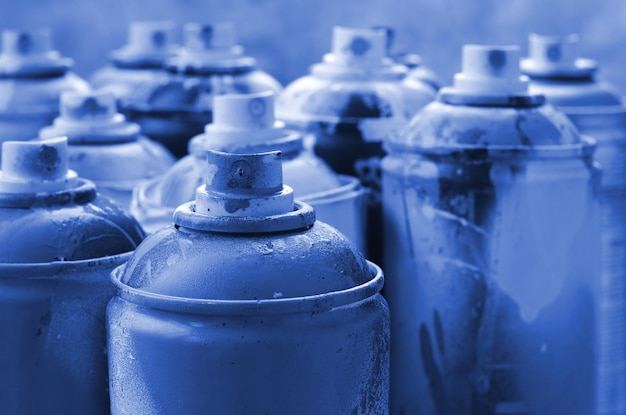 A lot of dirty and used aerosol cans of phantom classic blue colorpaint Macro photograph with shallow depth of field Selective focus on the spray nozzle