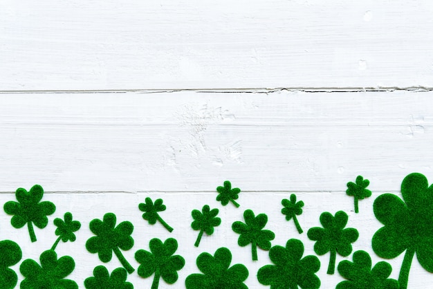 A lot of green paper clover leaf on white wooden background