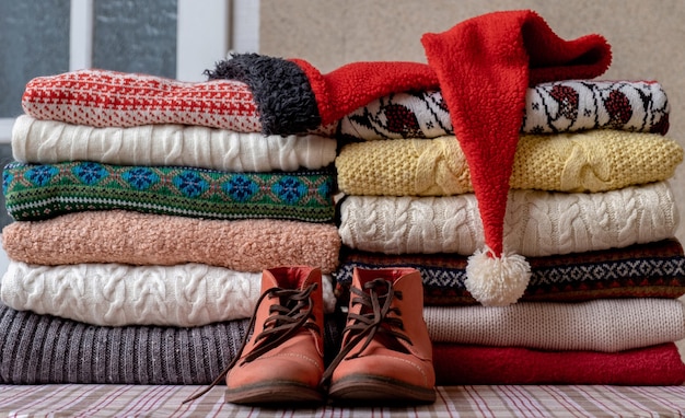 A Lot of Sweaters and Pullovers Different Colours folded in two Piles on the Table with old red shoes