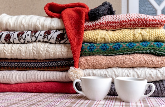 A Lot of Sweaters and Pullovers Different Colours folded in two Piles on the Table with two cups of coffee.