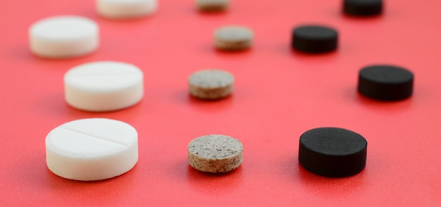 A lot of white, black and brown tablets lie on the red surface. 