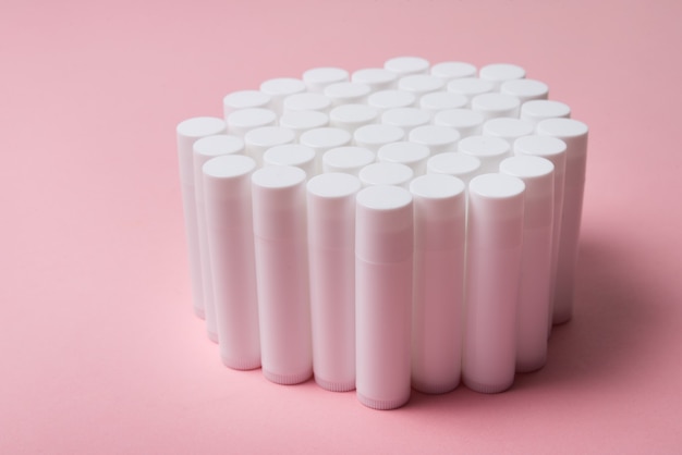 Lot of white plastic lip gloss tubes on pink background