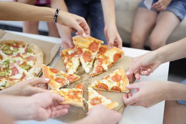 Lots of adults and childrens hands taking slices of delicious appetizing pizza closeup