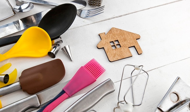 Lots of different kitchen utensils on the wooden table and a little wooden house between them