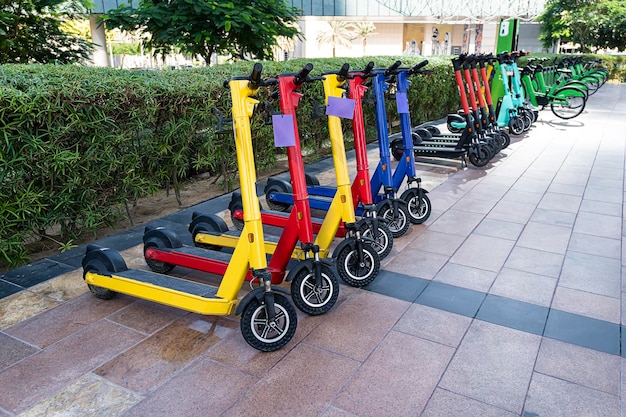 Lots of electric multicolored scooters in row on parking lot on asphalt City bike rental system public kick scooters on the street