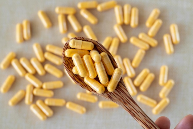 Lots of light yellow capsules in a wooden spoon on a white background Supplements vitamins medications or pills