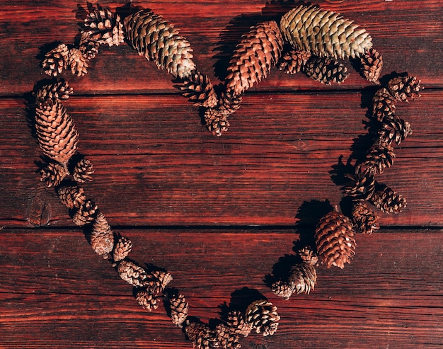 Photo lots of small pine cones lie in the shape of a heart on the wooden mahogany table