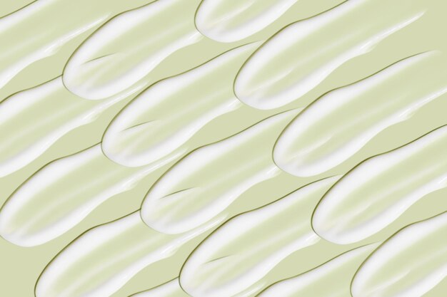 Lots of smears of cosmetic cream Light smooth surface In a row At an angle Top view Texture of flowing cream Liquid creamy strokes On green background Cosmetic background banner