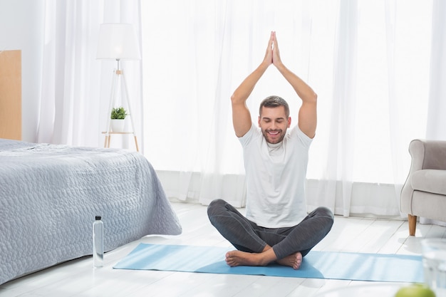 Lotus pose. Nice peaceful man holding his hands up while sitting in a lotus pose