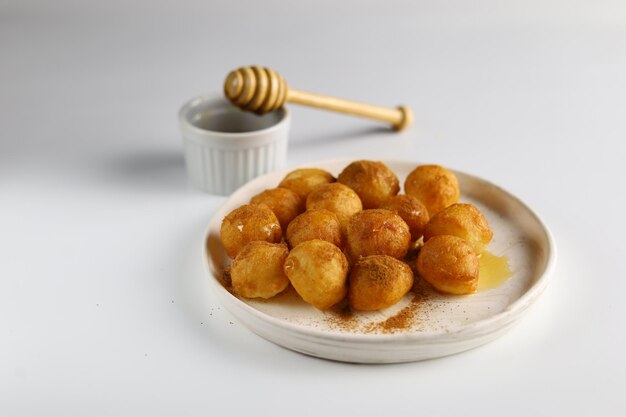 Photo loukoumades luqaimat or lokma with honey sauce in a plate with white background