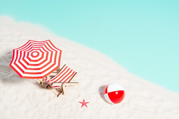 Lounge chair with parasol and beach ball on the coast, top view