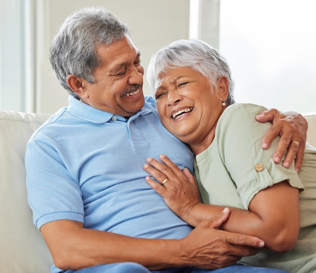 Love care and happy senior couple hugging each other while bonding and relaxing on sofa at home Elderly man and woman sitting on a couch in the living room while embracing talking and laughing