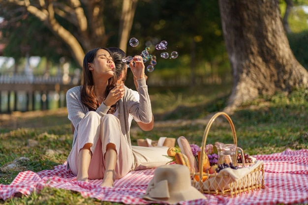 Photo in love couple enjoying picnic time blow soap bubbles in park outdoors picnic happy couple relaxing together with picnic basket