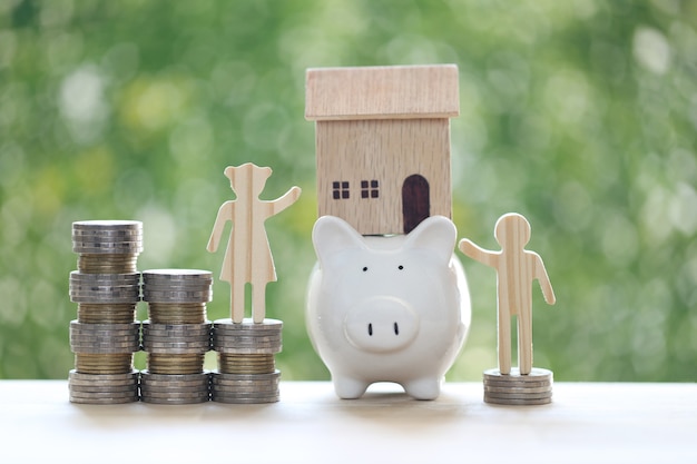 Love couple with model house on piggy bank and stack of coins money on natural green background