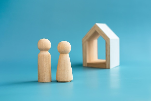 Love couple wooden figure model male and female symbol standing front of minimal white wood house on blue background Building family First home buying house real estate investment concept