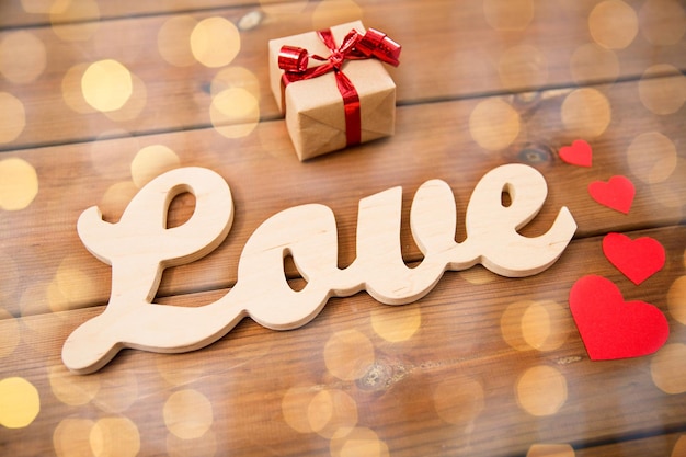 love, date, romance, valentines day and holidays concept - close up of word love with gift box and red hearts on wood