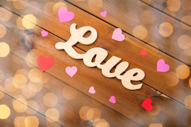 love, date, romance, valentines day and holidays concept - close up of word love with red and pink paper hearts on wood