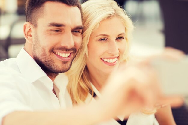 Photo love, date, technology, people and relations concept - smiling happy couple taking selfie with smatphone outdoors