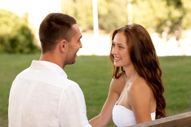 love, dating, people and friendship concept - smiling couple sitting on bench and looking to each other in park