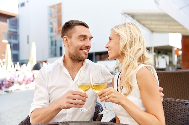 love, dating, people and holidays concept - happy couple drinking wine at open-air restaurant and clinking glasses