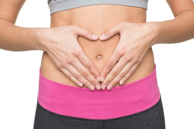 Love health. Cropped studio shot of a girl holding her hands in a shape of heart on her flat stomach wearing exercising clothing isolated on white