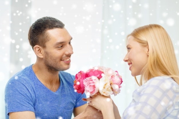 love, holidays, celebration, people and family concept - smiling man giving girlfriend flowers at home