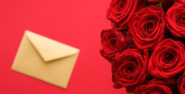 Love letter and flower delivery service on Valentines Day luxury bouquet of red roses and card envelopes on red background