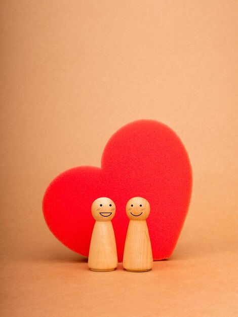 Love lover couple relationship LGBT Lesbian couple concept Two happy female wooden figures standing together on big red heartshaped sponge on eco brown kraft paper background for card or poster