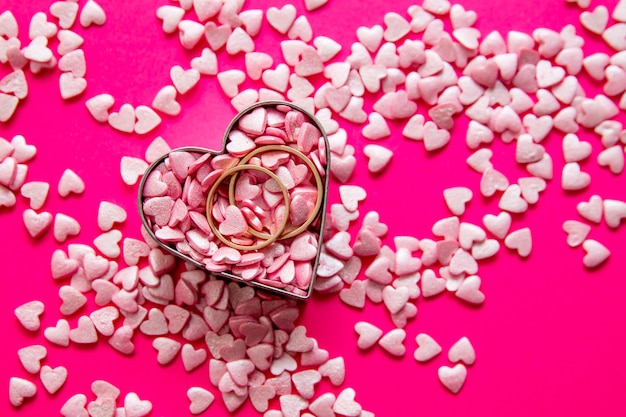 Love and marriage concept. Valentine's Day. Two golden wedding rings lying in a metal heart among lots of fair pink small hearts