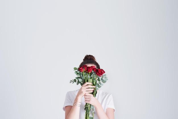 Love passionately like a red rose Studio shot of an unrecognizable woman covering her face with flowers against a grey background