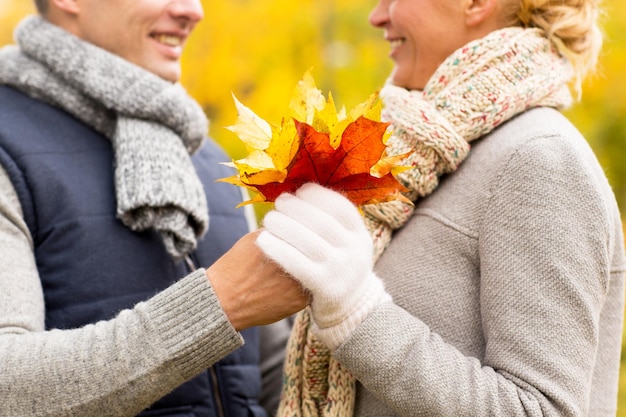 love, relationship, family and people concept - close up of happy smiling couple with maple leaves in autumn park