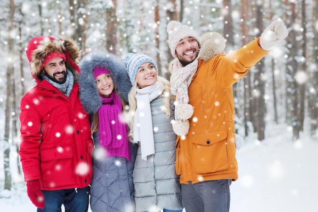 love, relationship, season, friendship and people concept - group of smiling men and women pointing finger in winter forest