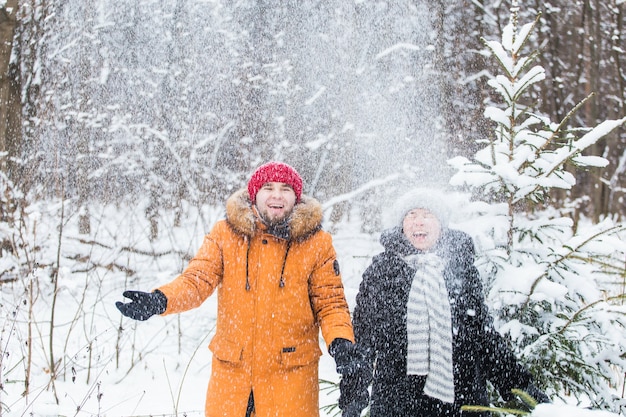 Love, season, friendship and people concept - happy young man and woman having fun and playing with snow in winter forest.