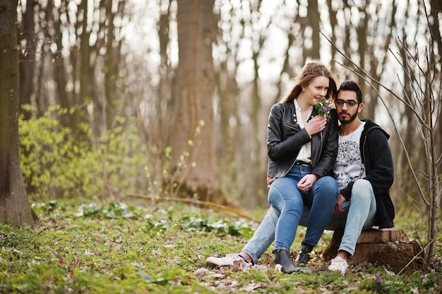 Love story of cool multiracial couple in spring forest They sitting on stump