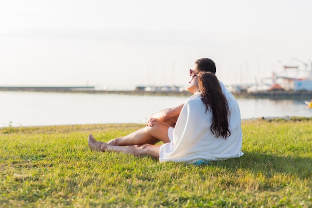 love, summer, dating and people concept - close up of happy couple sitting on grass at seaside