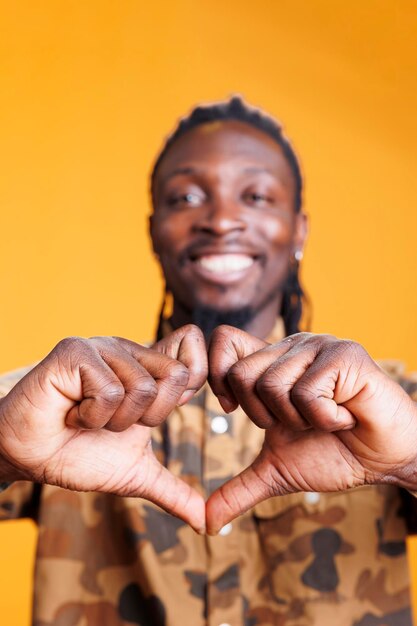 Lovely african american man making romantic gesture, doing heart shape with hands in studio over yellow background. Cheerful positive person showing affection and emotion, doing love sign