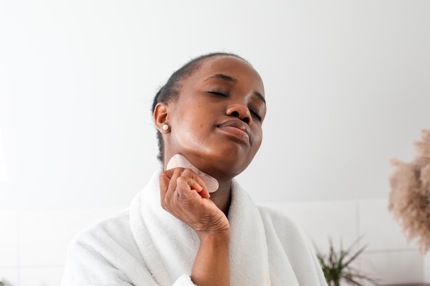 Lovely african girl massaging face with rose quartz gua sha