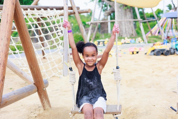 Lovely african girl play swing in playground summer camp learning