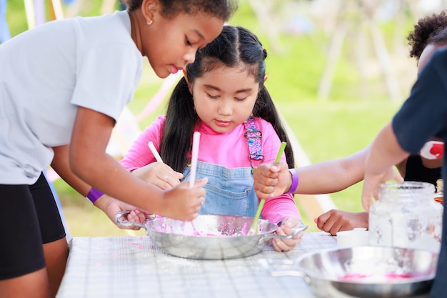 Lovely Asian and African girls playing dough together at playground summer camp learning